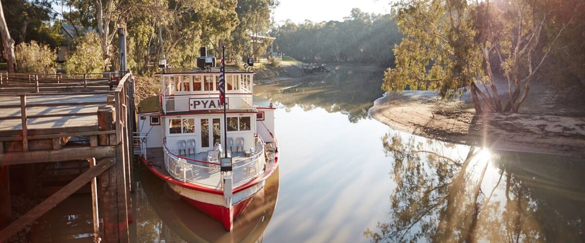 A riverboat docked at a pier with a forested riverbank.