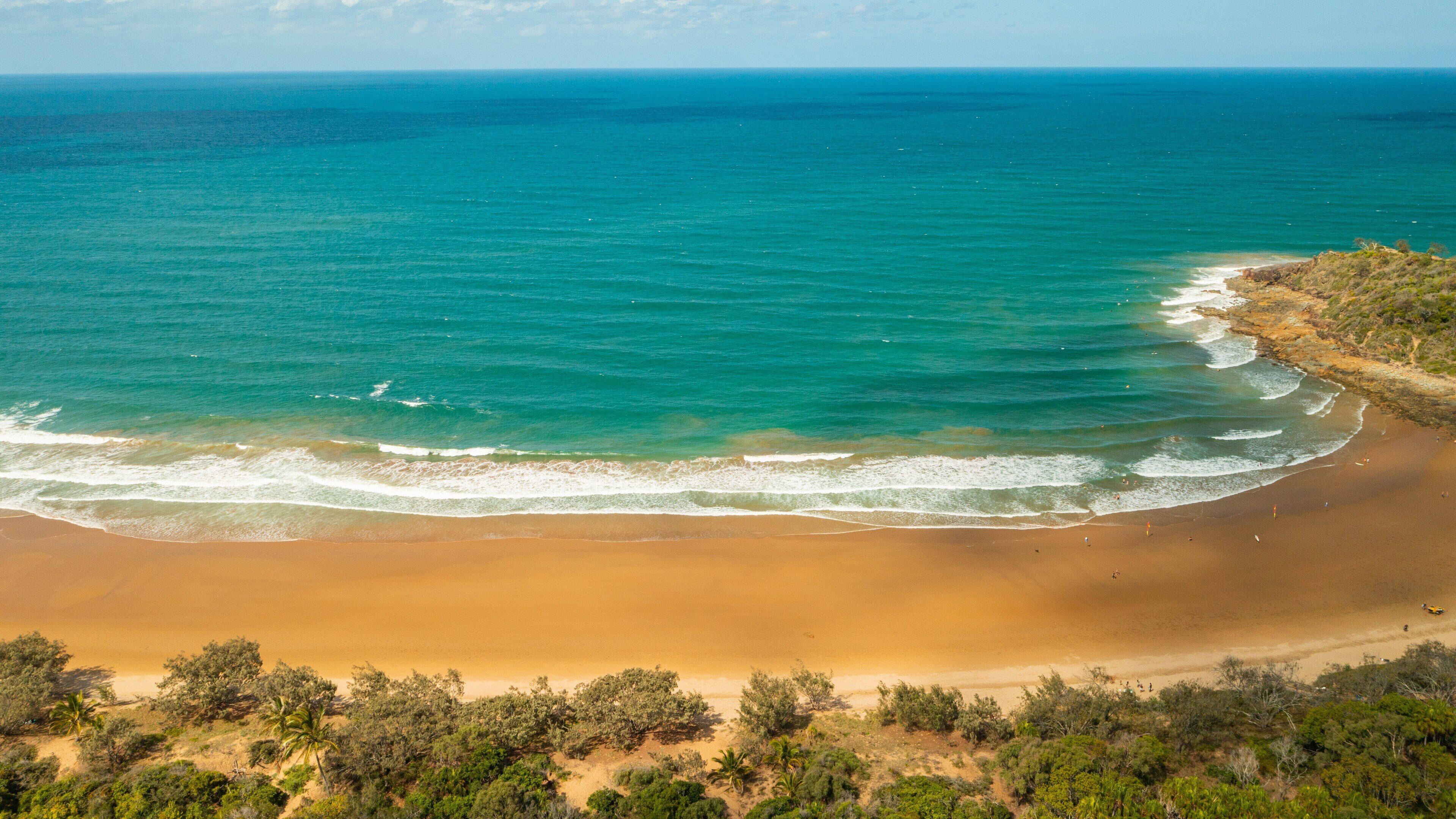 A coastal landscape with a sandy beach, turquoise ocean, and sparse vegetation.