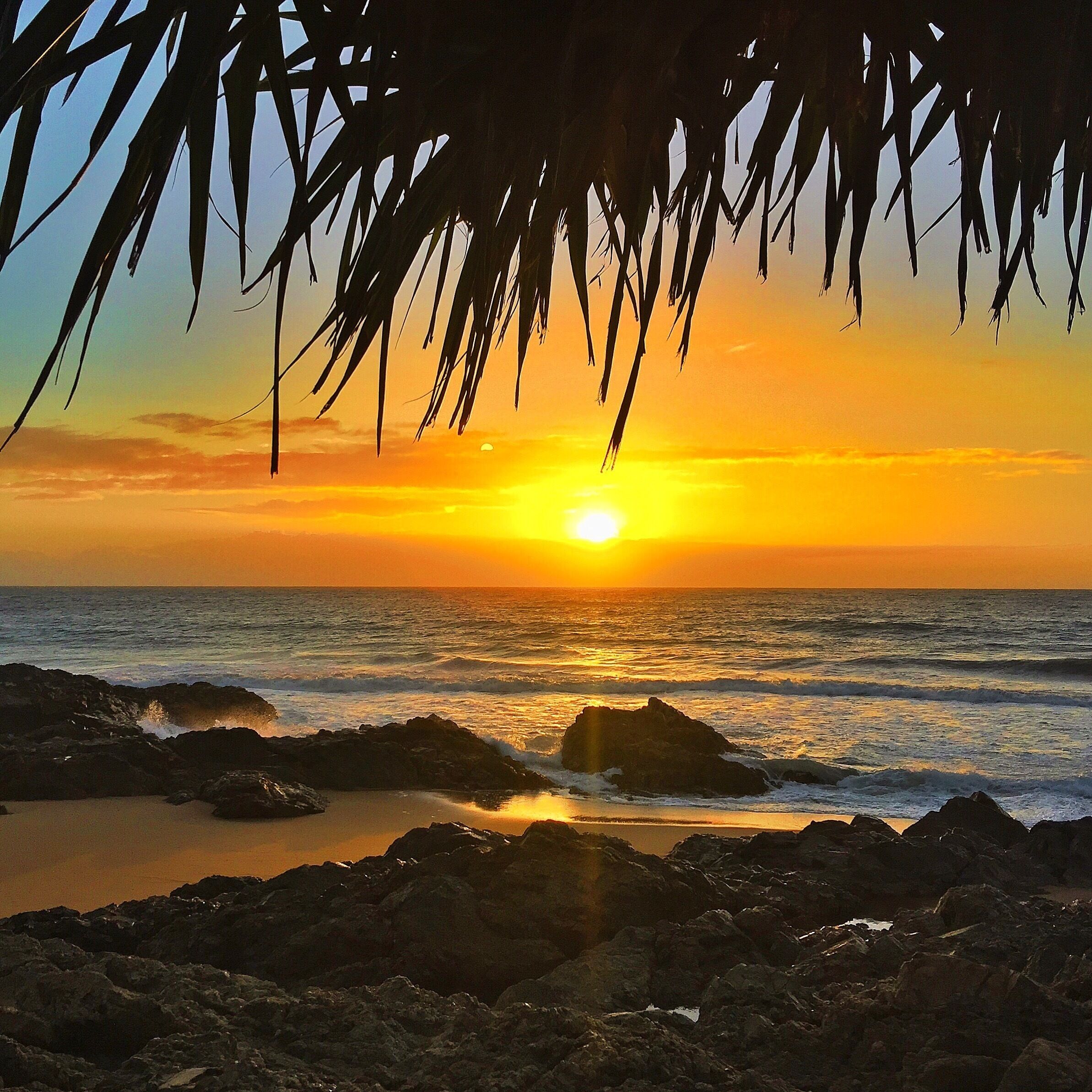 A sunset over a rocky coastline with waves crashing against the shore.