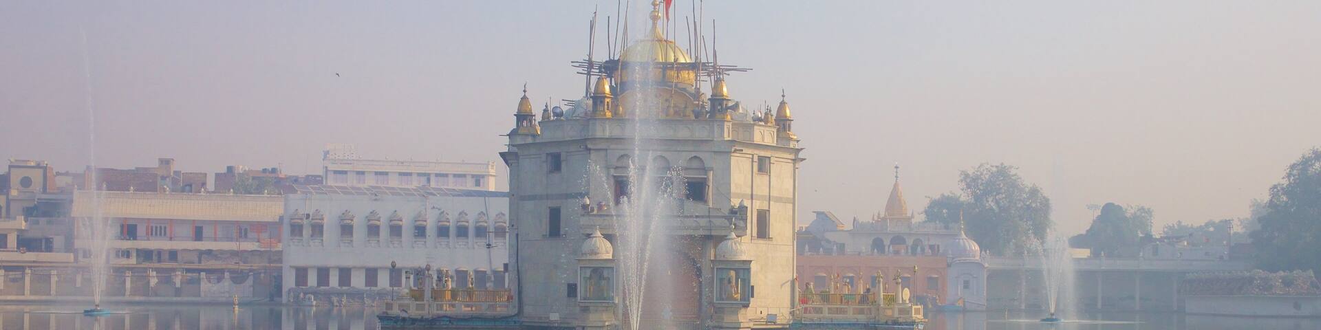 A historic building with a golden dome and a flag, surrounded by calm water and other structures.