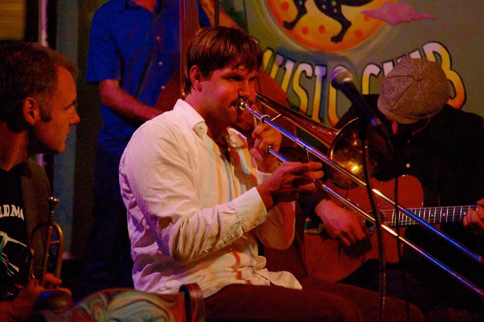 A brass instrument player in a dimly lit venue with a colorful mural in the background.