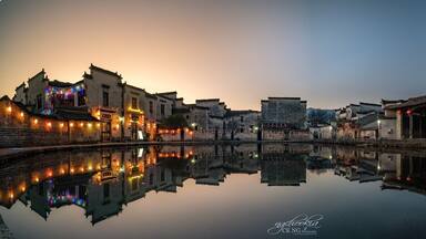 Un tranquilo pueblo a orillas del río al anochecer, con edificios iluminados que se reflejan en el agua.