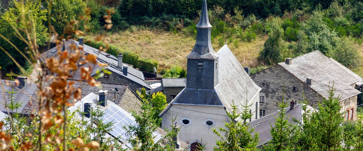 A church with a pointed steeple surrounded by lush greenery and trees.