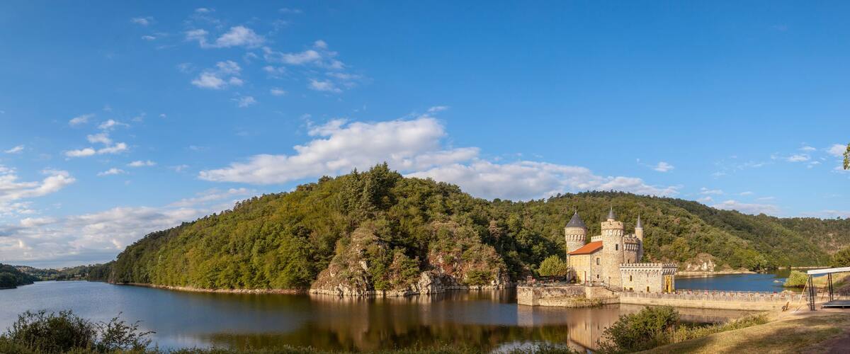 A castle by a lake surrounded by forested hills.