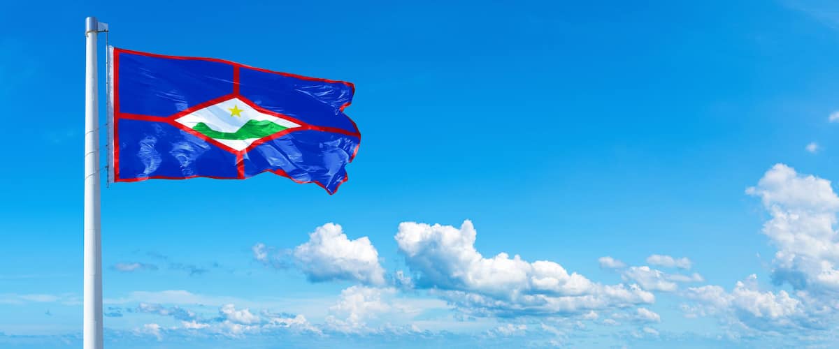A flag on a pole against a blue sky with clouds.
