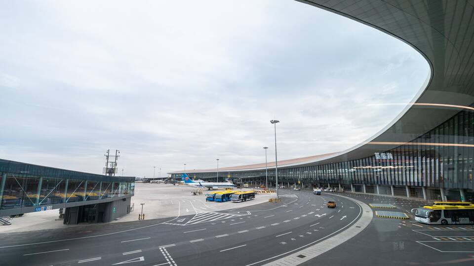 An airport terminal with curved architecture, a clear sky, and a road with directional arrows.