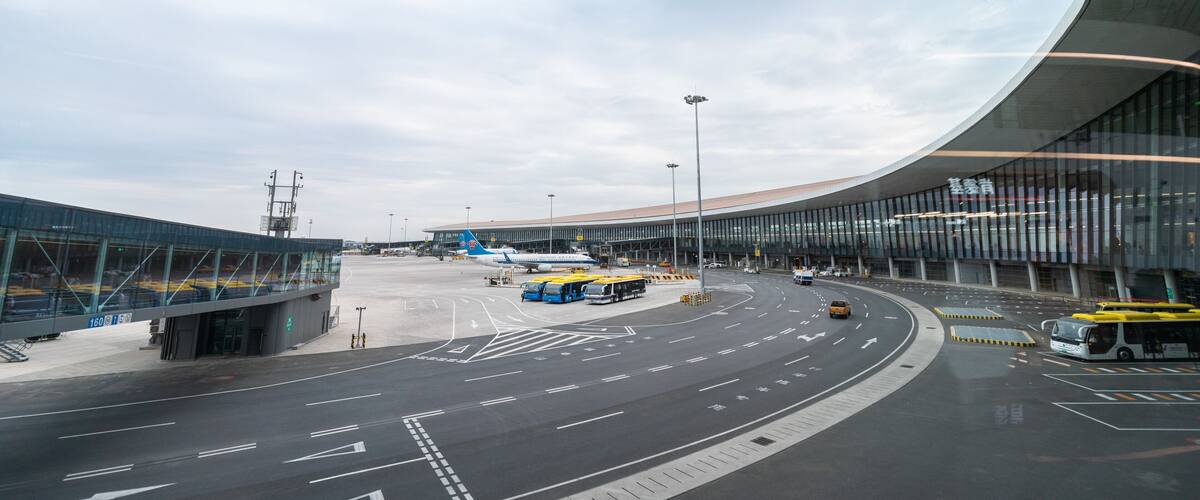 An airport terminal with curved architecture, a clear sky, and a road with directional arrows.
