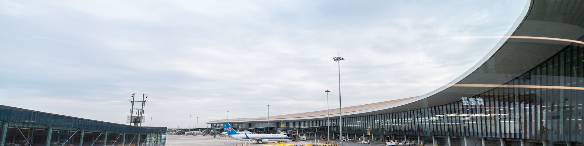 An airport terminal with curved architecture, a clear sky, and a road with directional arrows.