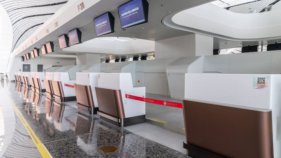 A modern airport terminal with check-in counters, digital screens, and a polished floor.