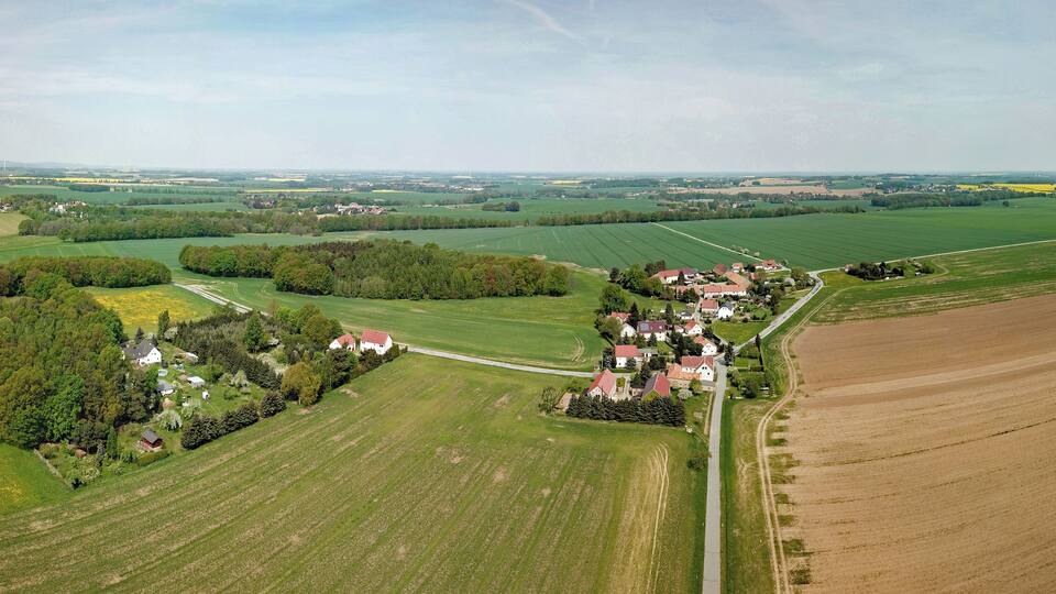 An aerial view of a rural landscape with fields, a cluster of houses, and a road.