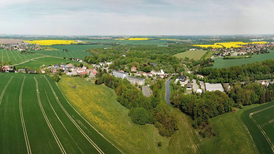 An aerial view of a rural area with fields, a small village, and a river.