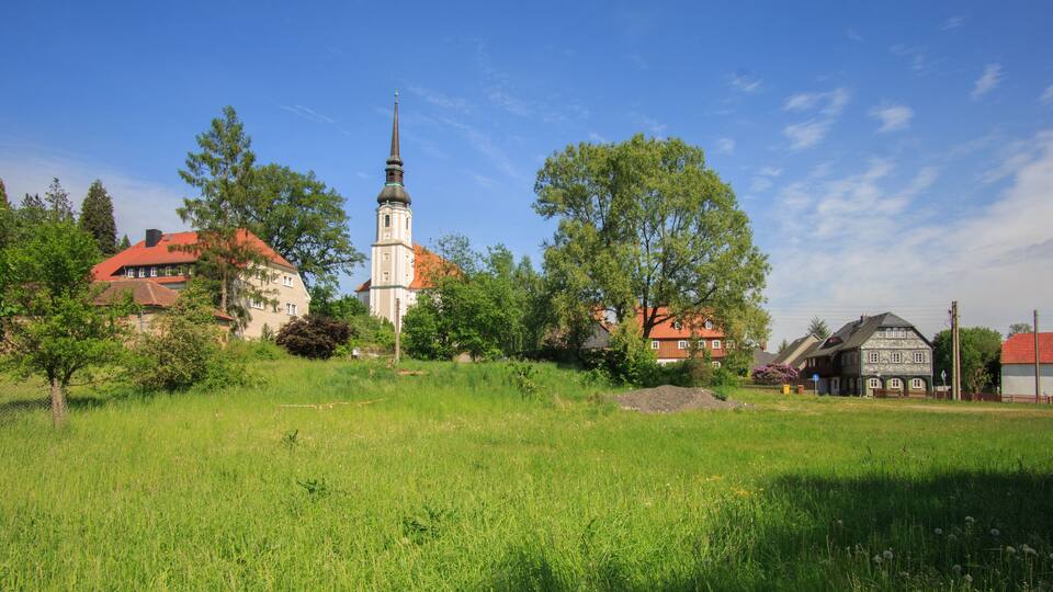 A church with a tall spire, surrounded by lush greenery and residential buildings.