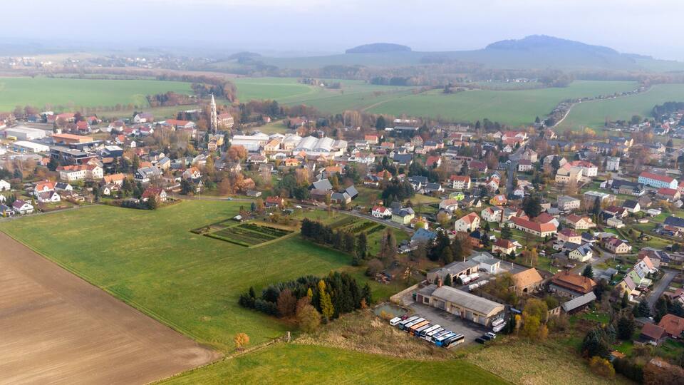 An aerial view of a town with a prominent church, green fields, and residential areas.