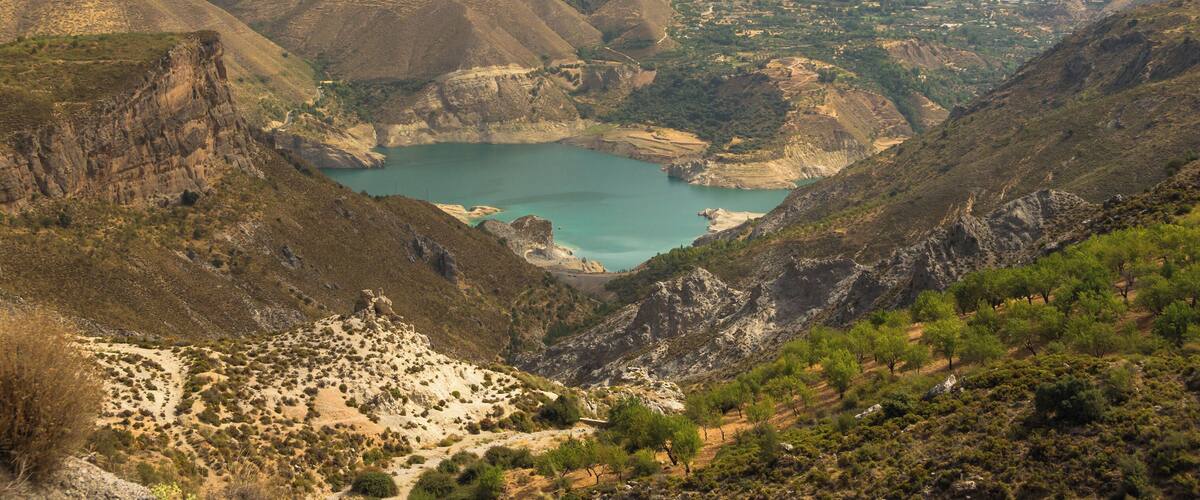 A mountainous landscape with a turquoise lake surrounded by rugged terrain and sparse vegetation.