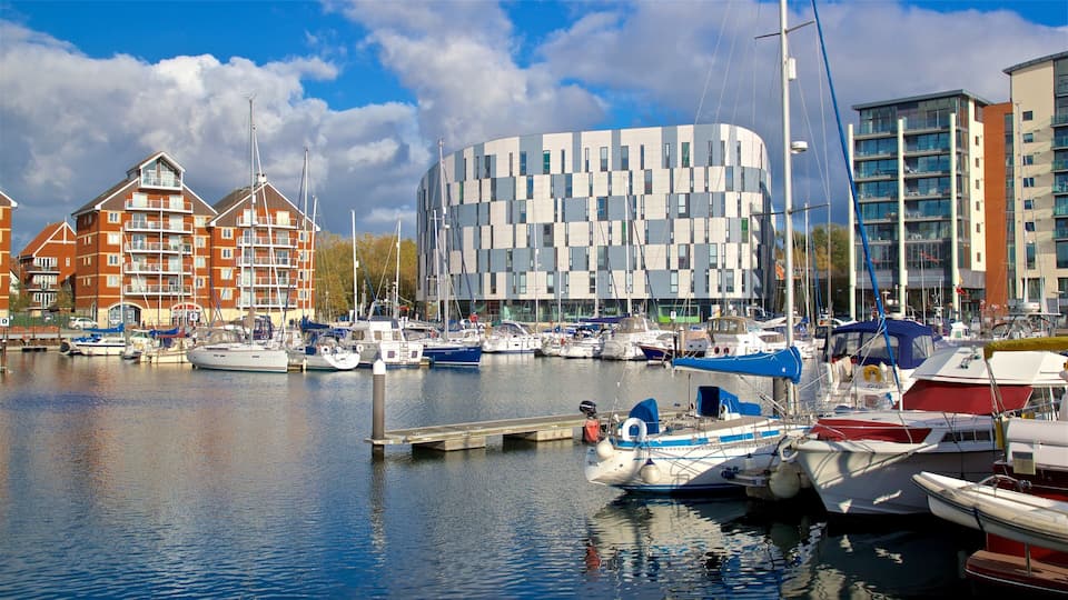A marina with boats docked, a modern building with a unique facade, and traditional red brick buildings in the background.