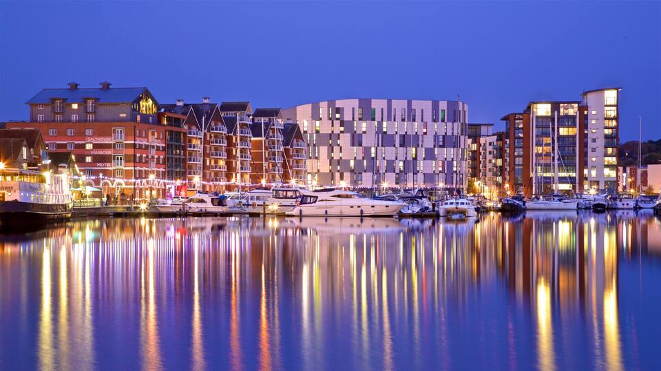 A marina with boats and buildings reflecting on the water at dusk.