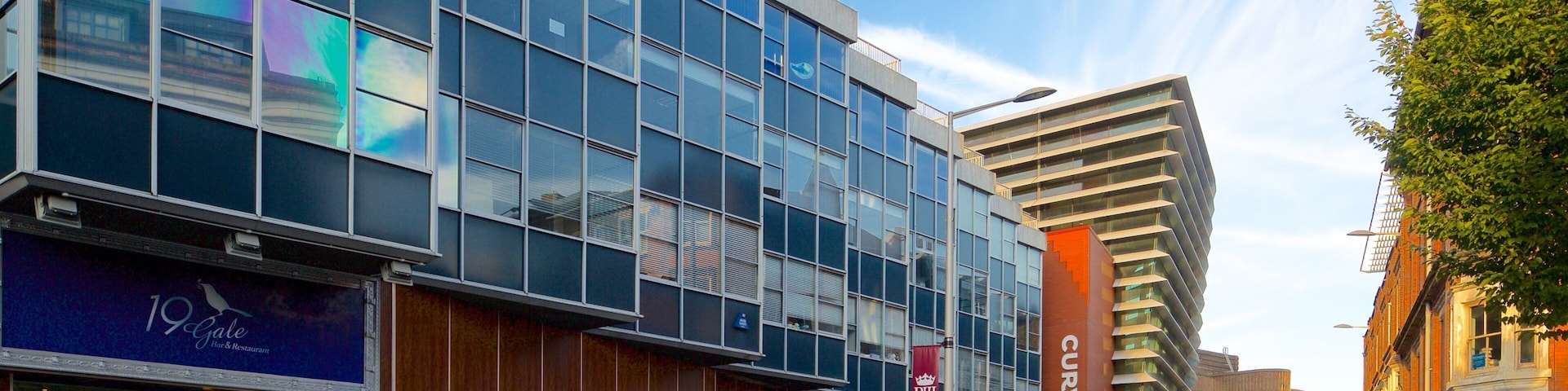 A modern urban street with a mix of commercial buildings, including a restaurant named '19 Gate' and a building with 'CURVE' signage.