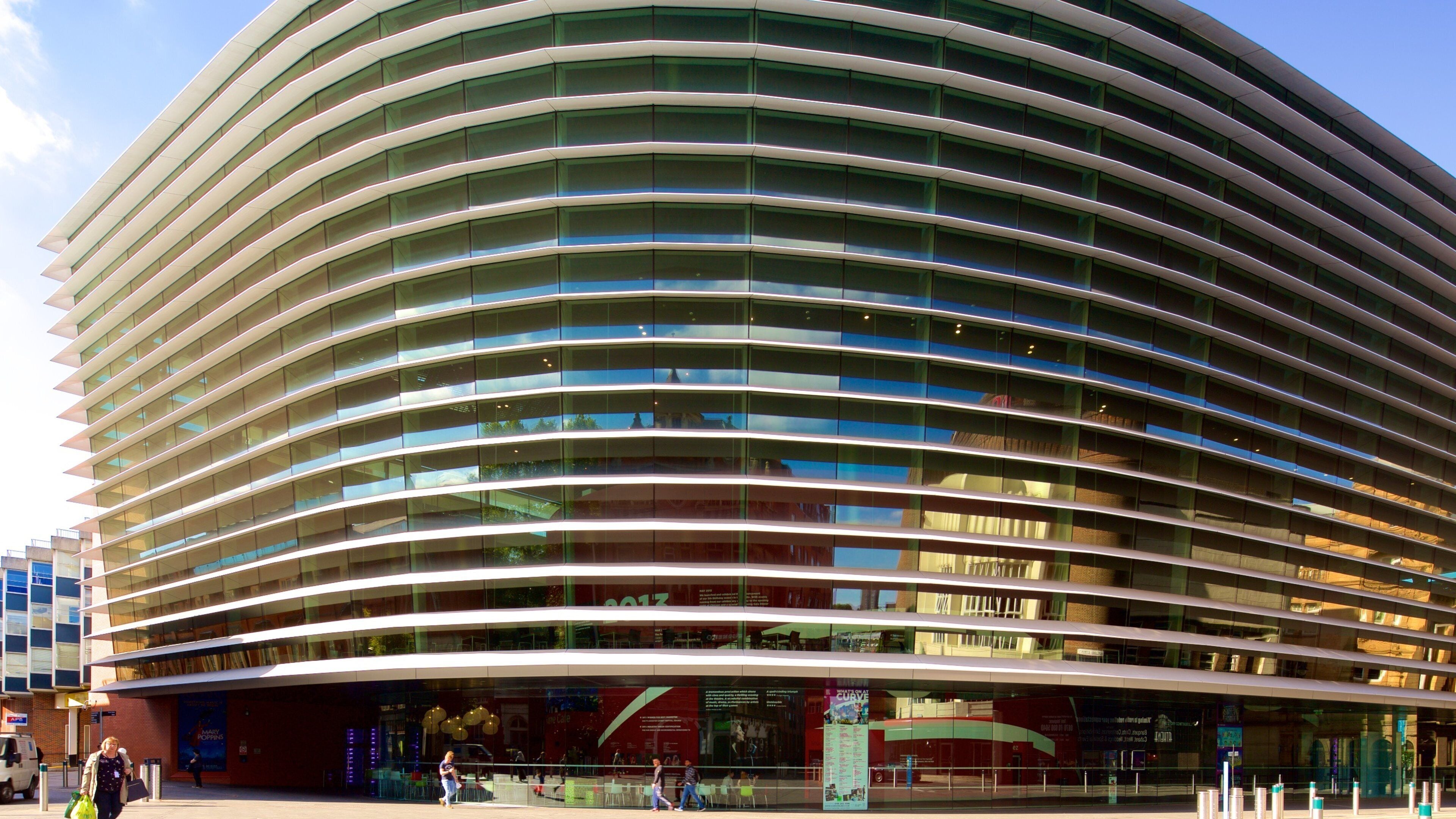 A modern curved building with horizontal glass windows and a red advertisement on the lower level.