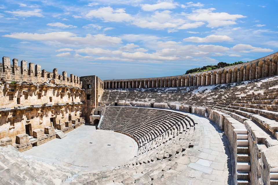 Un anfiteatro antiguo con asientos de piedra y un escenario central.