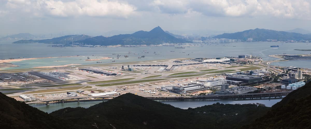 An airport with multiple runways, a large body of water, and mountains in the background.