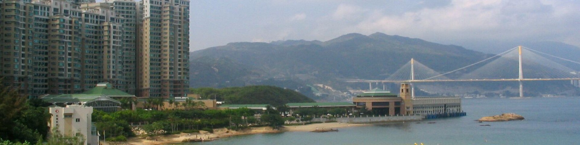 Paisagem costeira com edifícios altos, uma ponte e uma praia.