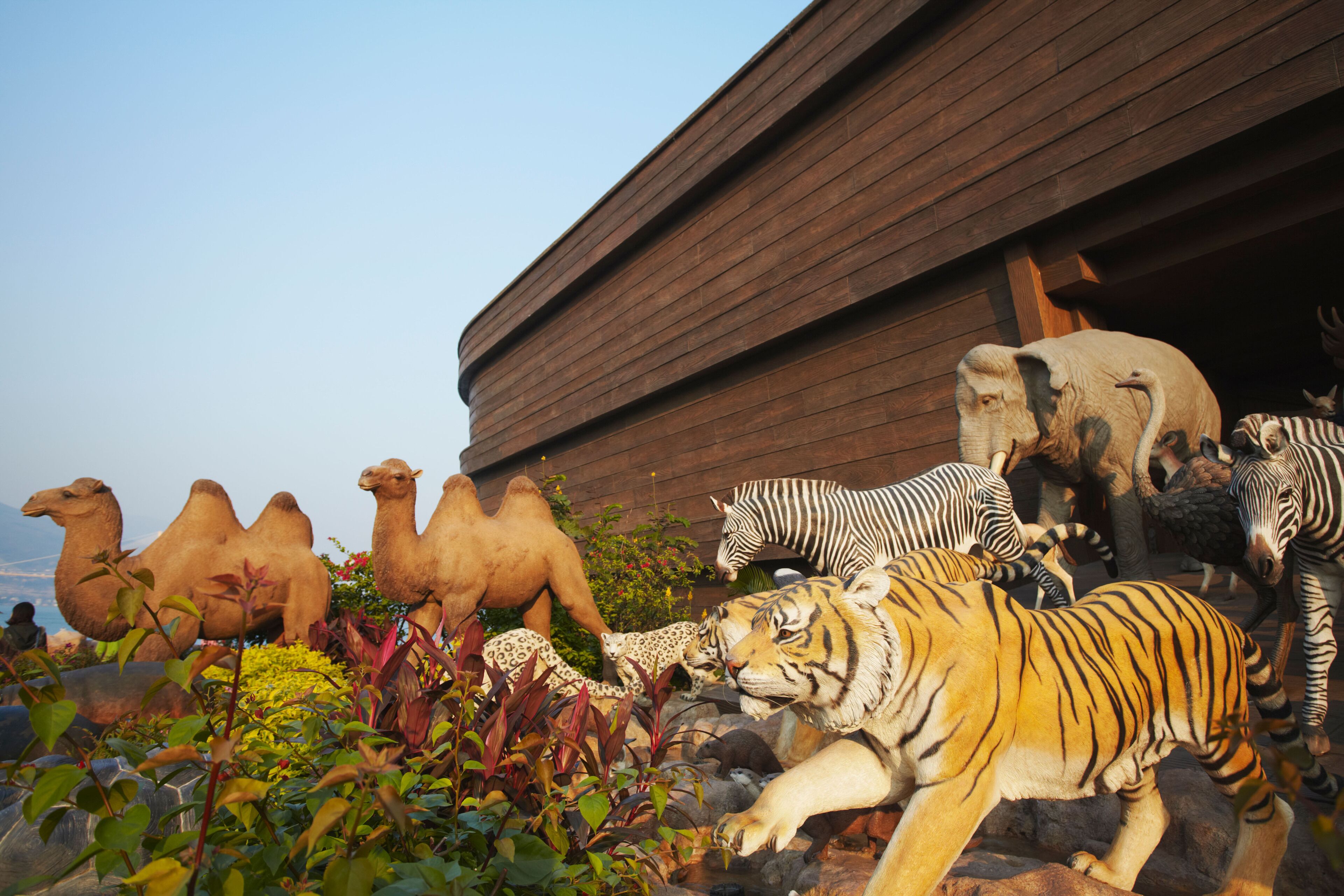 Varias esculturas de animales, incluyendo camellos, cebras, un tigre y un rinoceronte, frente a un edificio de madera.