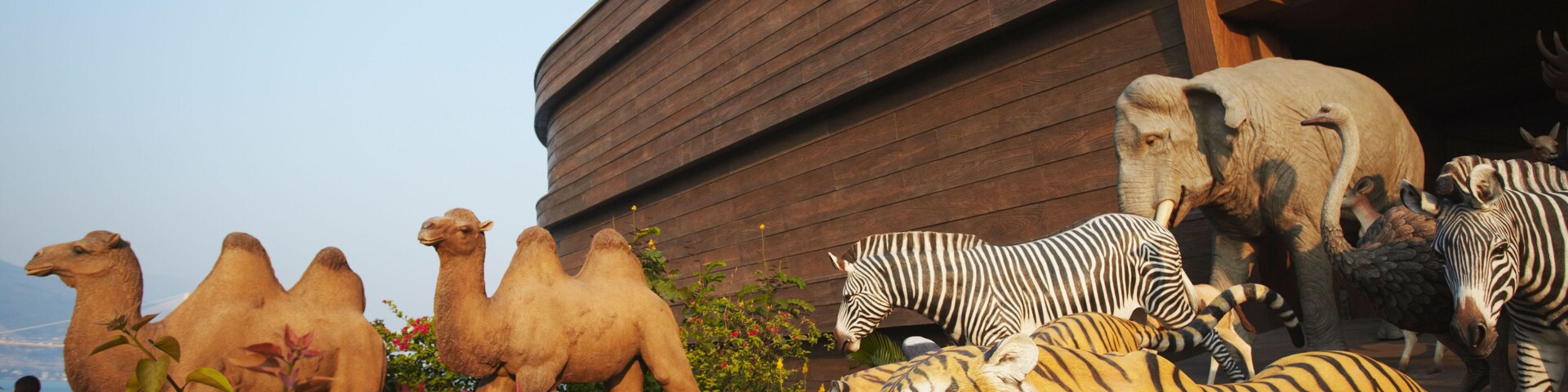 Varias esculturas de animales, incluyendo camellos, cebras, un tigre y un rinoceronte, frente a un edificio de madera.