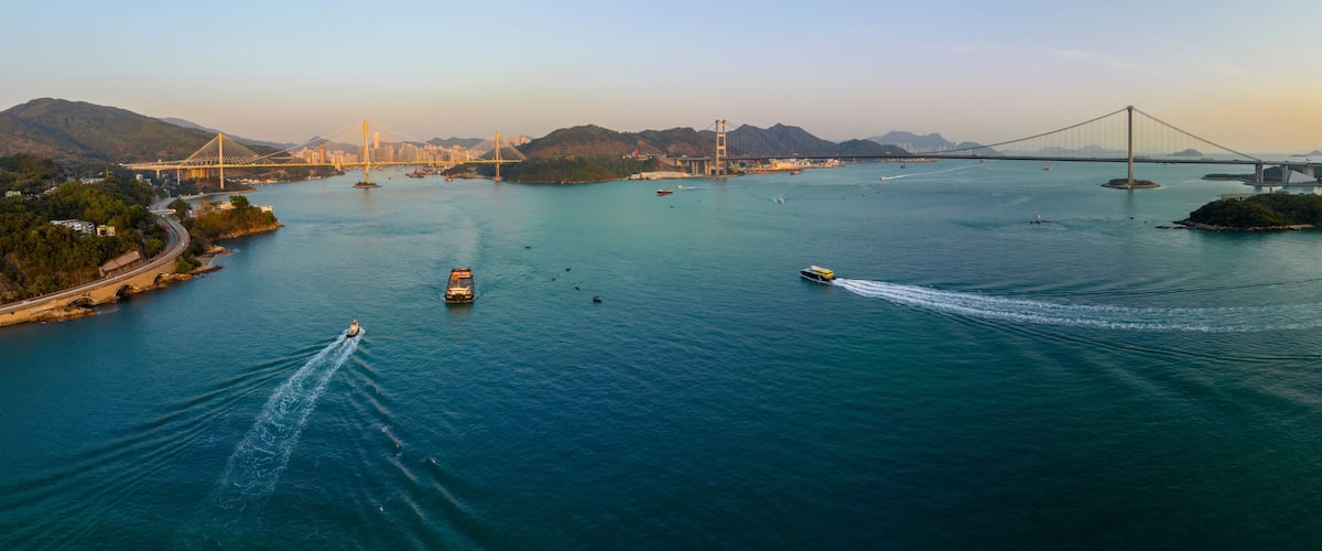 A river with boats, a bridge, and a cityscape with mountains in the background.