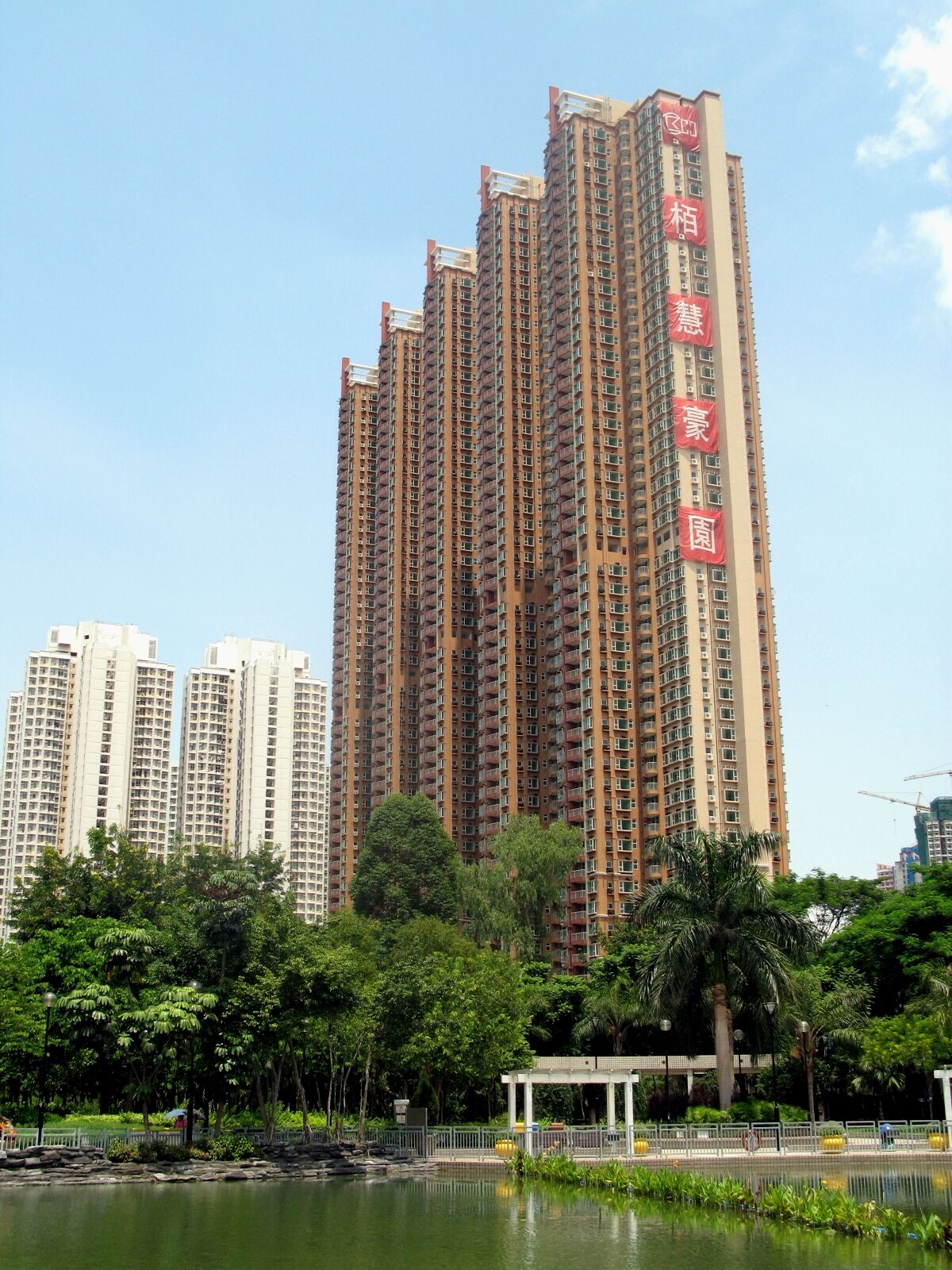 A high-rise residential building with multiple balconies and a large pond in the foreground.