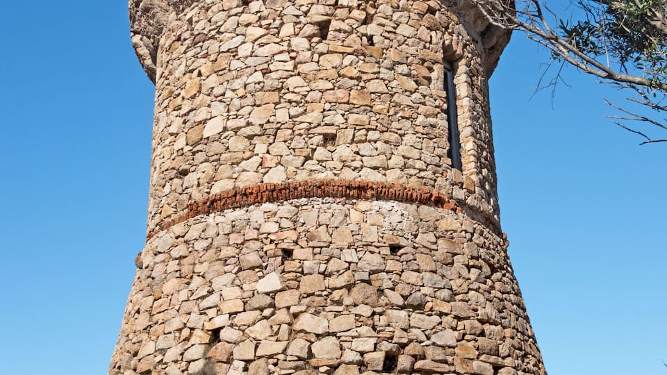 A stone tower with a circular base and a narrow top, surrounded by sparse vegetation.