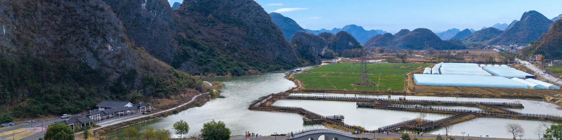 Un río con un puente, un paisaje montañoso y campos verdes.