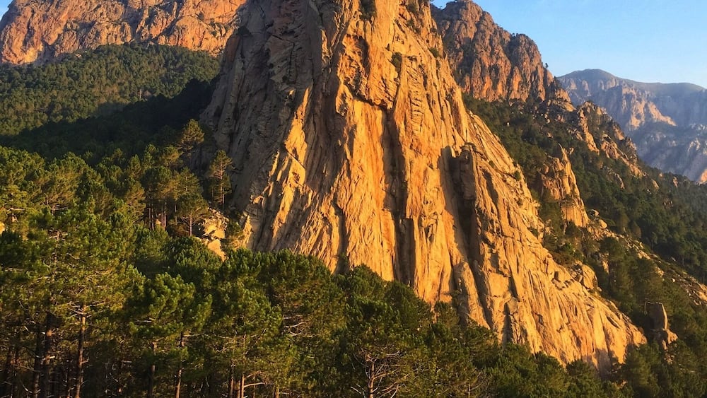Un sommet montagneux escarpé, avec une forêt au premier plan et un ciel bleu dégagé.