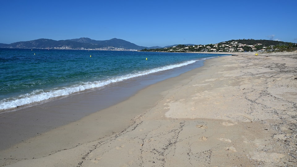 A sandy beach with gentle waves, a clear blue sky, and distant mountains.