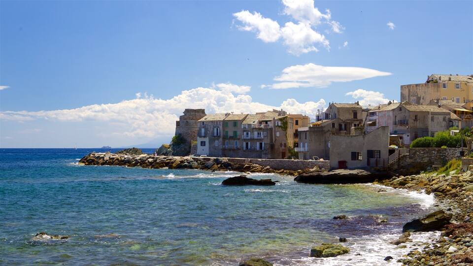 A coastal town with stone buildings, clear blue sea, and rocky shoreline.