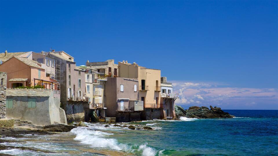 A coastal town with buildings built on stilts over the water, a rocky shoreline, and clear blue skies.