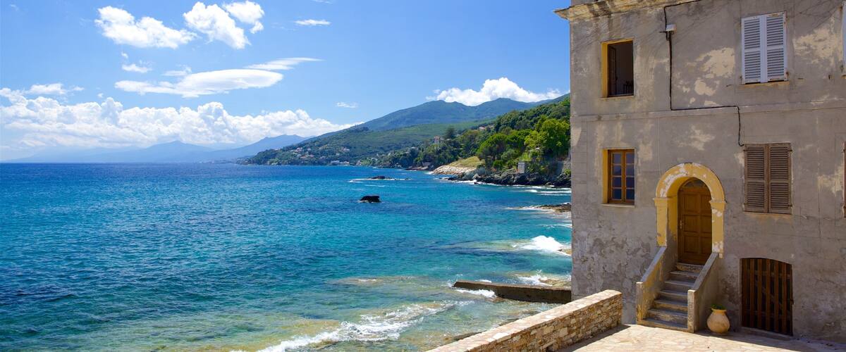 A coastal building with a clear view of the sea and a mountainous backdrop.