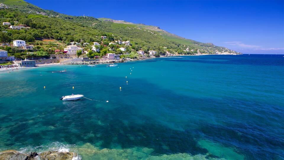 A coastal town with clear turquoise waters, a boat anchored near the shore, and buildings on a hillside.