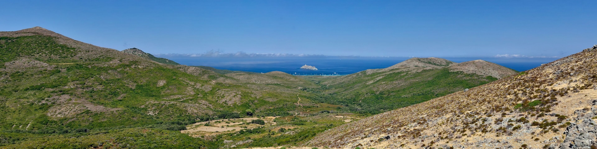 A mountainous landscape with a valley and a distant view of the sea.