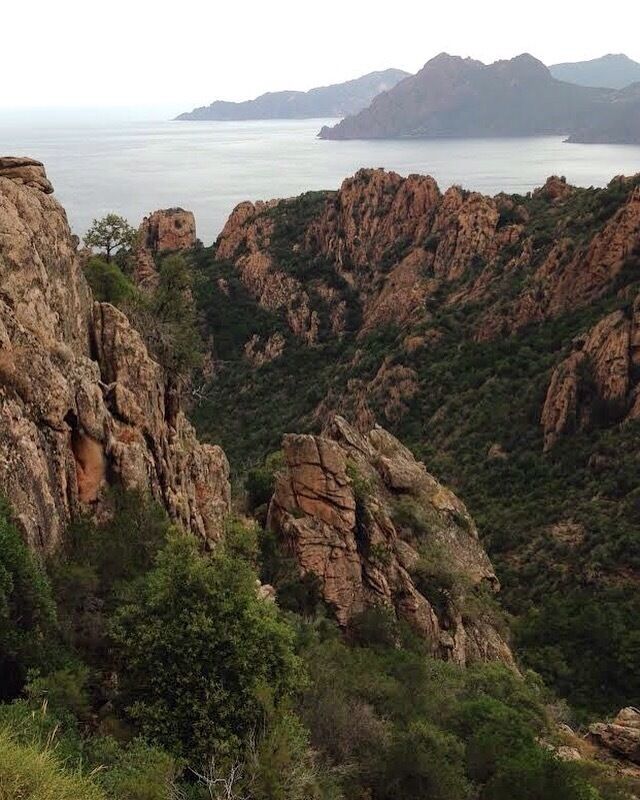Rugged cliffs, dense greenery, and a distant body of water.