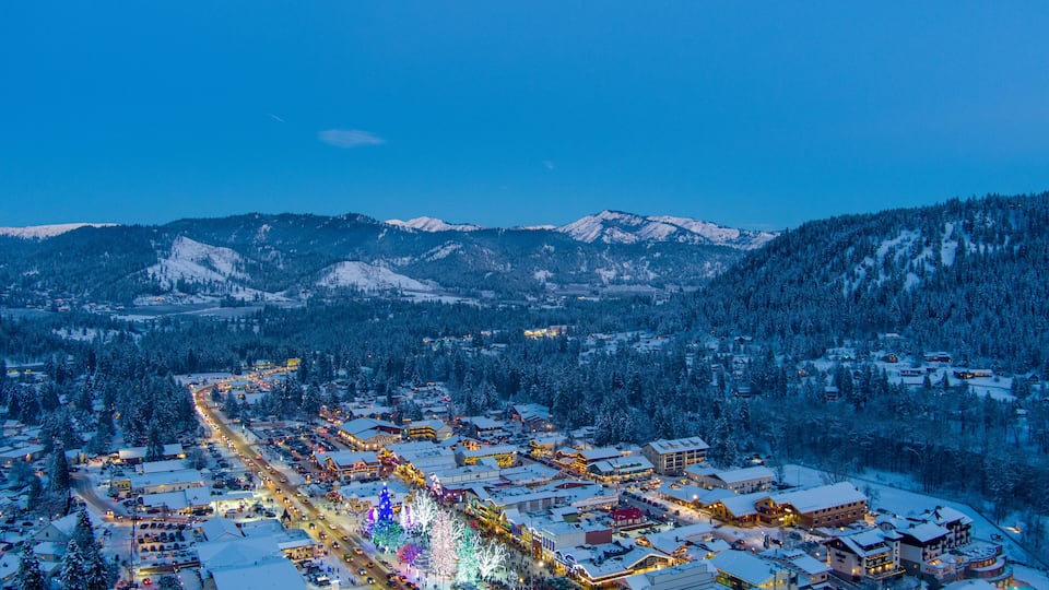A snow-covered town with illuminated buildings and a mountain backdrop.