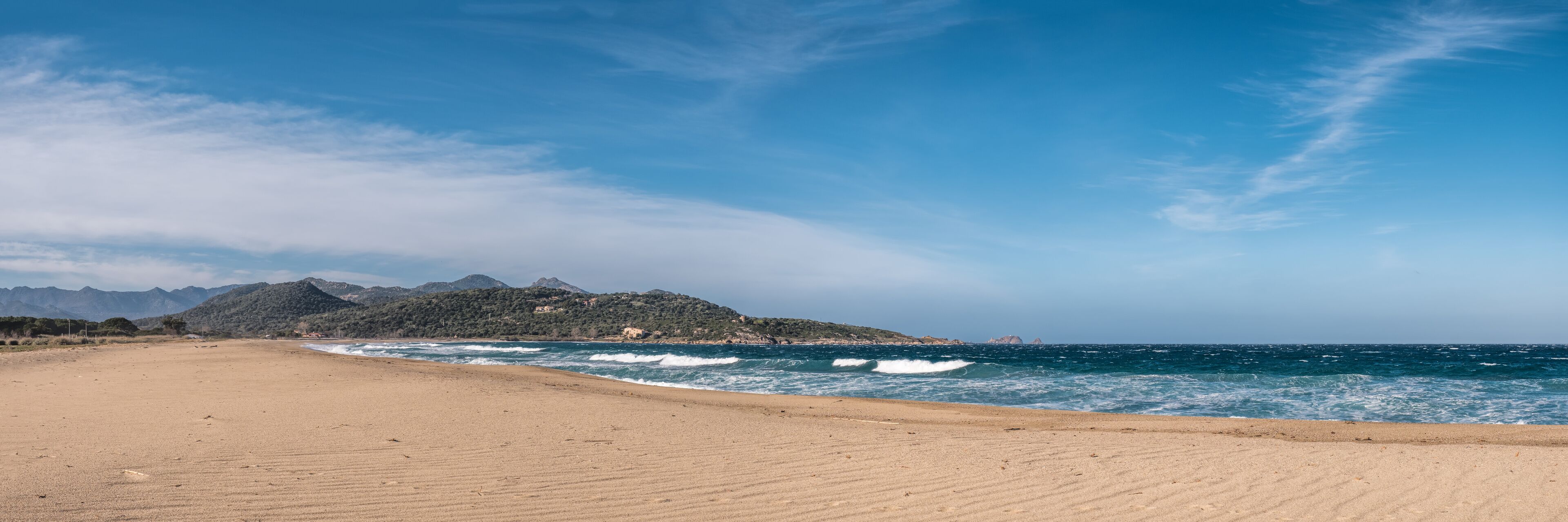 A beach with a clear sky, waves, and mountains in the background.