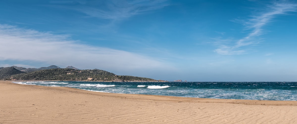 A beach with a clear sky, waves, and mountains in the background.