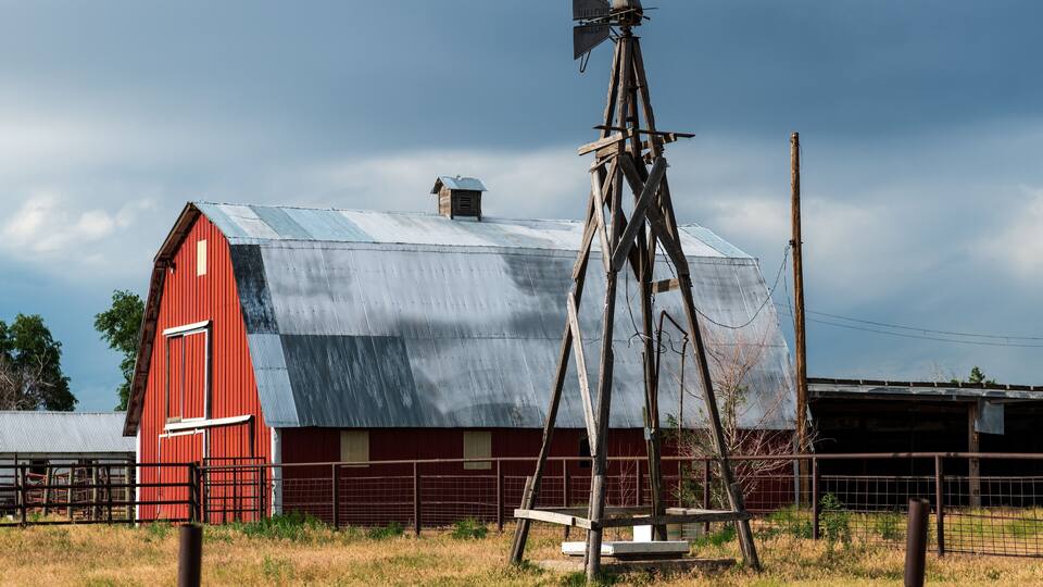 A red barn with a weather vane, a metal roof, and a fence in a rural setting.