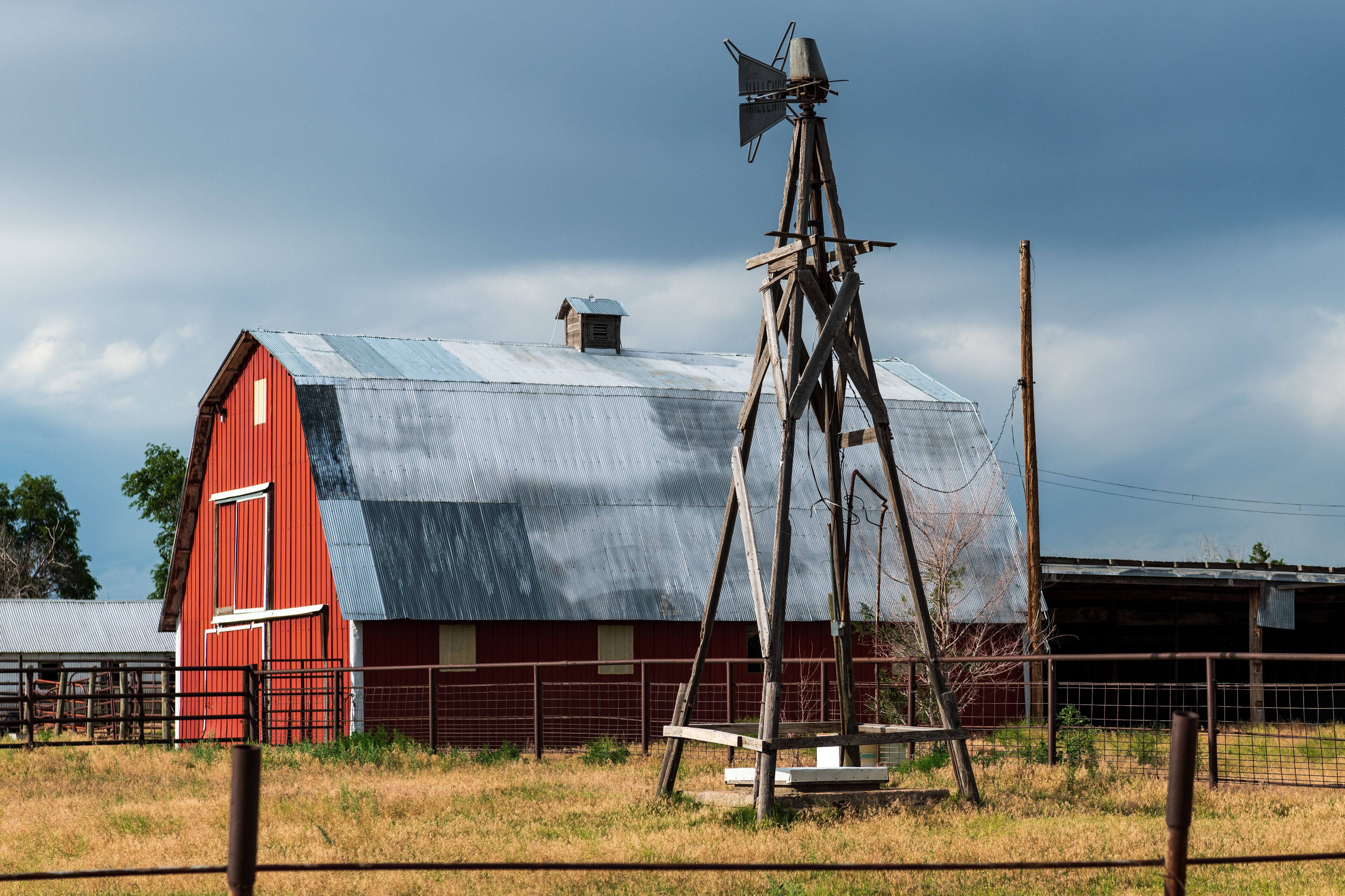A red barn with a weather vane, a metal roof, and a fence in a rural setting.