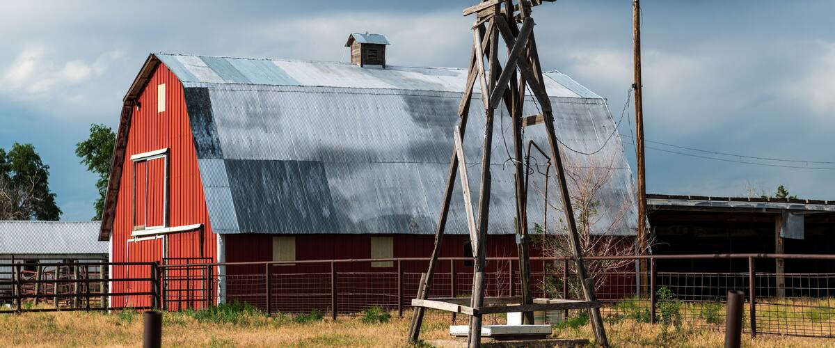 A red barn with a weather vane, a metal roof, and a fence in a rural setting.