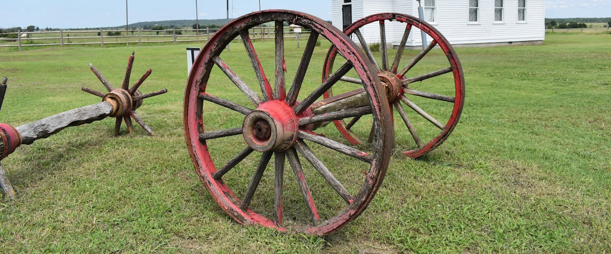 A white building labeled 'Sunny Side' with two large, red-painted wooden wheels in a grassy field.
