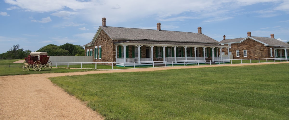 A historic brick building with a covered porch and a red carriage in front.