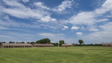 A grassy field with a row of brick buildings and a flagpole with an American flag.