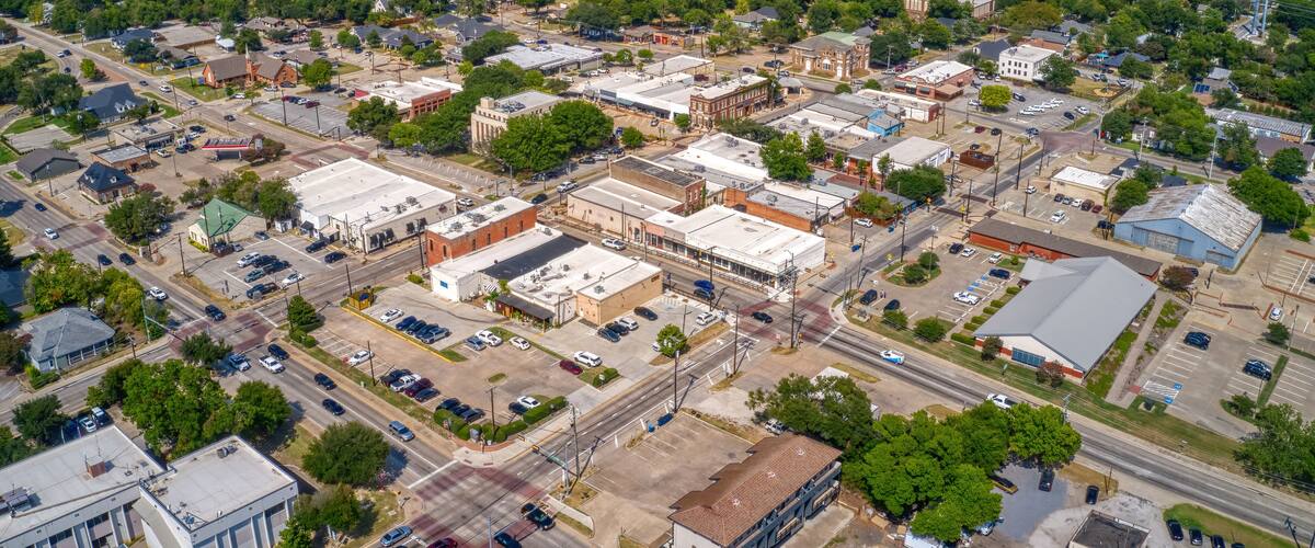 An aerial view of a town with a mix of commercial and residential buildings, roads, and green spaces.