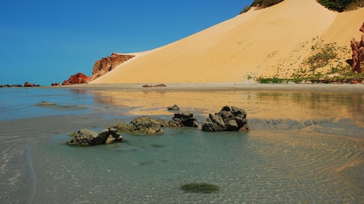Ein Strand mit klarem Wasser, Sanddünen und Felsformationen.
